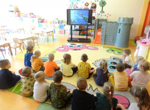 Grupa dzieci ogląda prezentację multimedialną na temat dinozaurów.
